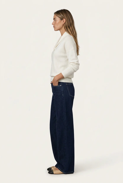 Side view of the Menielle Antonine Sweater in white: knit sweater with a V-shaped shawl collar and ribbed cuffs, with dark jeans